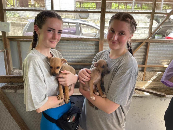 Two girls stood smiling at the camera both holding puppies.
