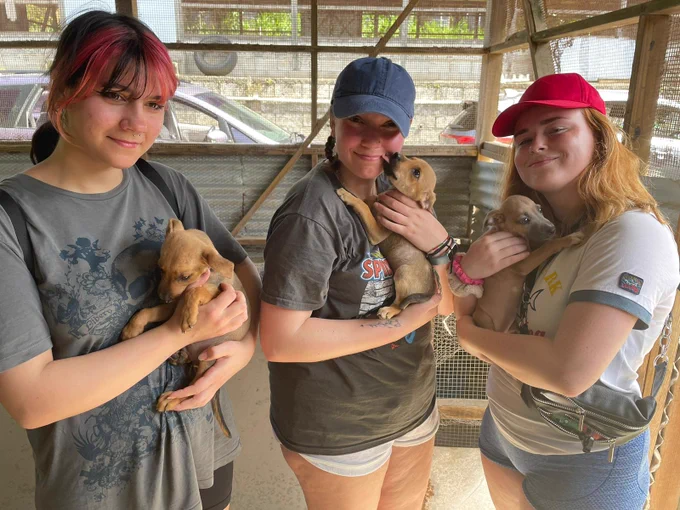 Three female students stood smiling at the camera holding three puppies.