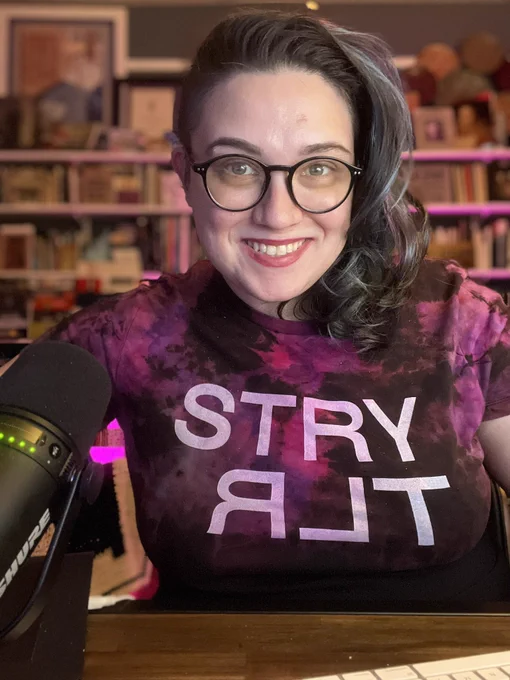 Emily Friedman smiles at camera while wearing an ice-dyed T-shirt that reads STRYTLR — or storyteller without vowels