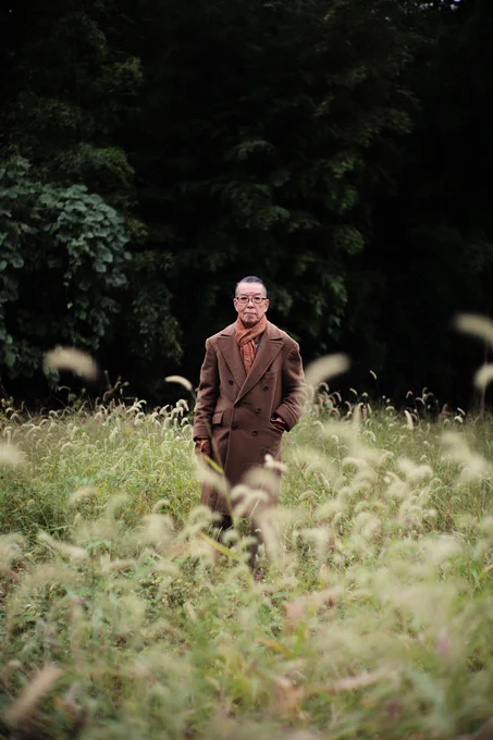 Yukio Akamine wears a brown double-breasted Ulster coat with an orange paisley scarf