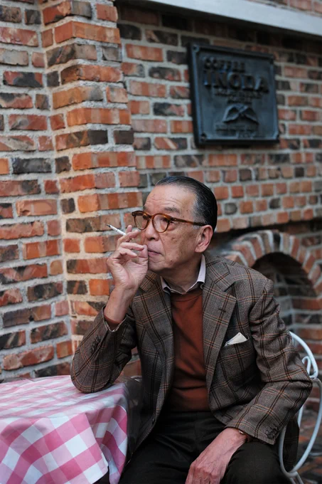 Yukio Akamine wears a brown checked, single-breasted tweed with a rust-colored crewneck sweater, white dress shirt, and charcoal wool trousers. 
