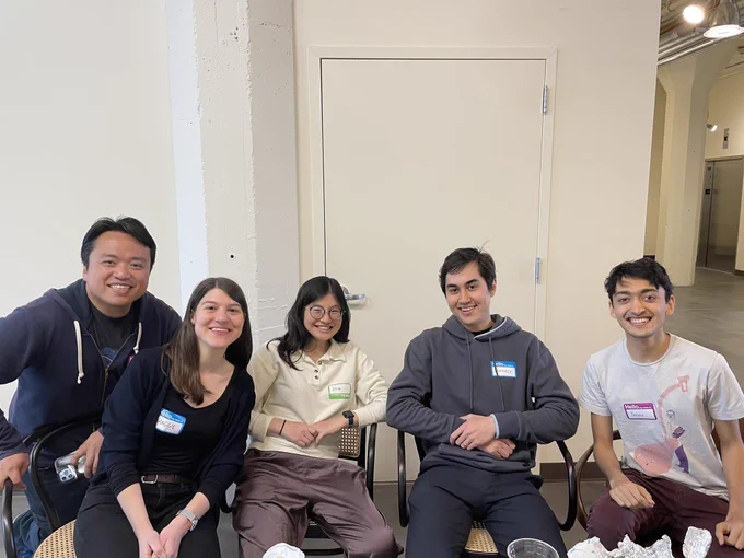 Five people sitting in a row wearing stick-on name tags, smiling less bracingly this time!