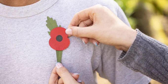 A plastic-free poppy being pinned onto the the left breast of a person wearing a grey t-shirt.