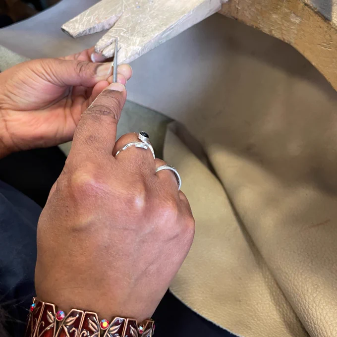 a pair of hands works at a wooden jewellers peg on a small piece of tubing