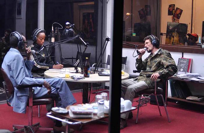 Three people sitting around a round table speaking into microphones, recording 
