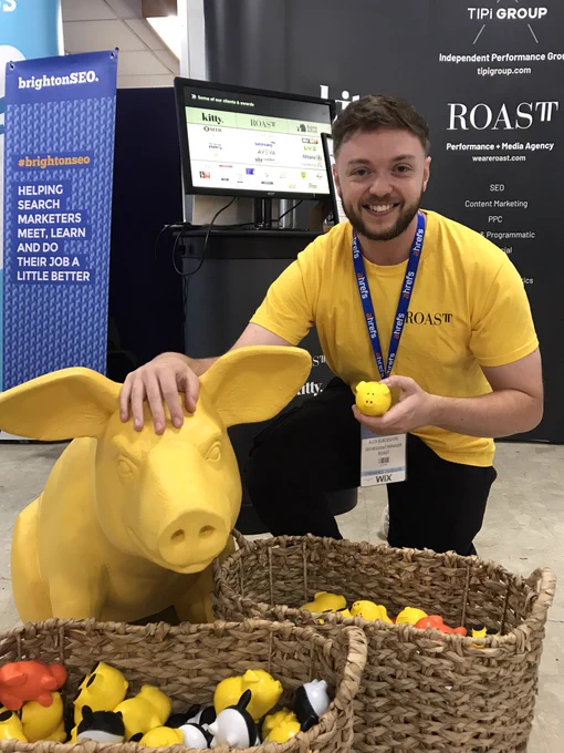 Someone holding a small pig toy crouching by a bigger pig statue