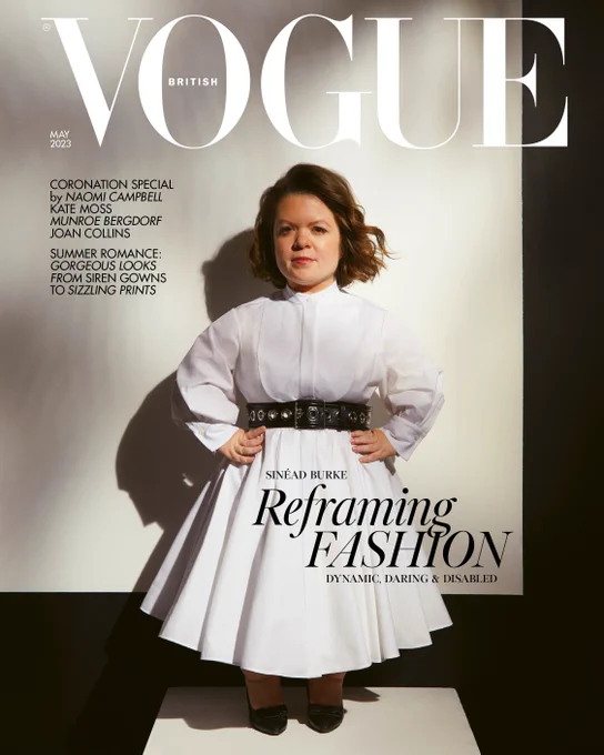 Image shows Sinéad Burke, a white, queer little person, on the cover of British Vogue. Sinéad’s brown bob has been curled into soft waves that are blowing gently in the wind. With both of her hands resting on her hips, she stands against a white backdrop, wearing a white shirt dress with a black belt by Alexander McQueen, and her own black, pointy pumps by Ferragamo. Above her head, a white Vogue logo in big letters. The cover also reads ‘Reframing Fashion: Dynamic, Daring & Disabled.’