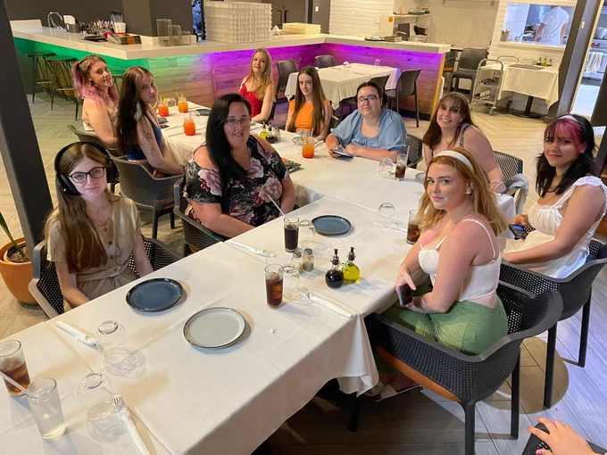 Students sat smiling at the camera. They are sat at a table with white table cloth with plates and drinks set out in front of them.