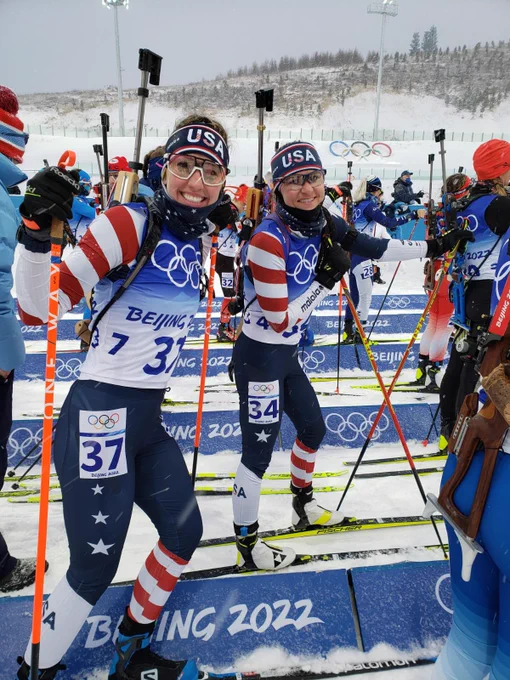 Deedra stands on her skis smiling ready to start the biathlon race at the 2022 Beijing Winter Olympics.