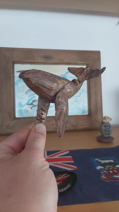 A small wooden figure of a whale in motion - it could fit in the palm of your hand. The wood is dark with visible carving lines that accentuate the feeling of movement.