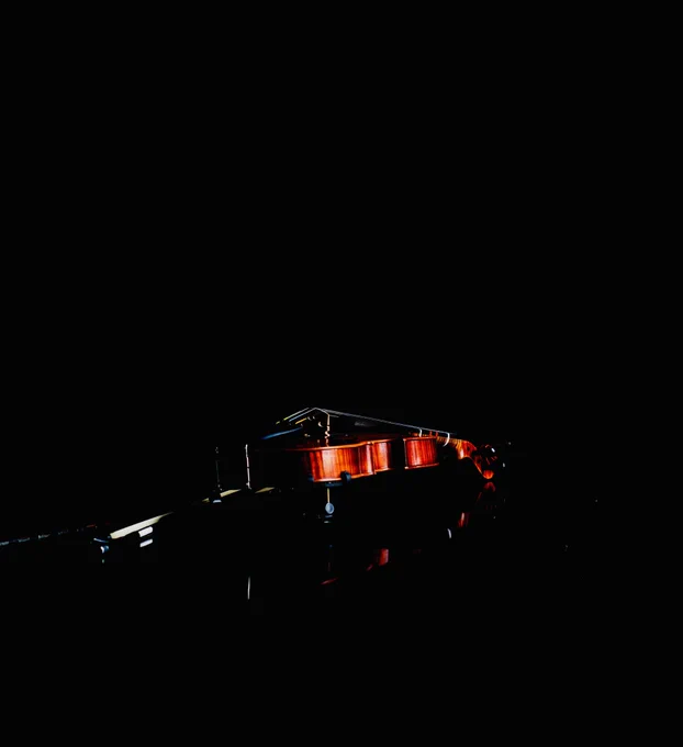 An overexposed still of a photo (by Elliott Tilliczek x SA Smythe). Photo of a violin laying flat in what appears to be a reflective black lacquered atmosphere.