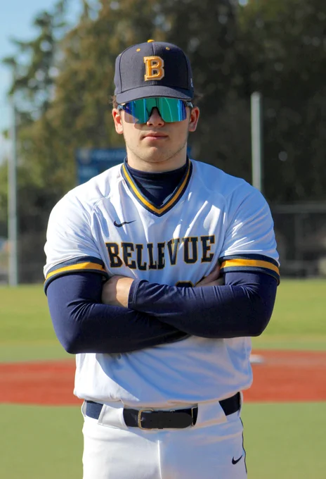 Jackson Hyatt, a baseball player, stands in the field with his arms folded, and wearing sunglasses.
