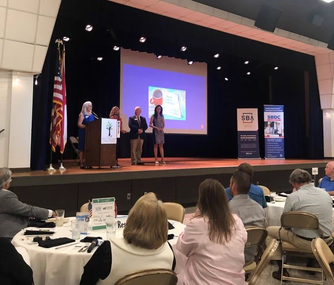 Photo of SBDC Director, DDD, L.D. Ralph, and 2 winners on stage receiving awards.