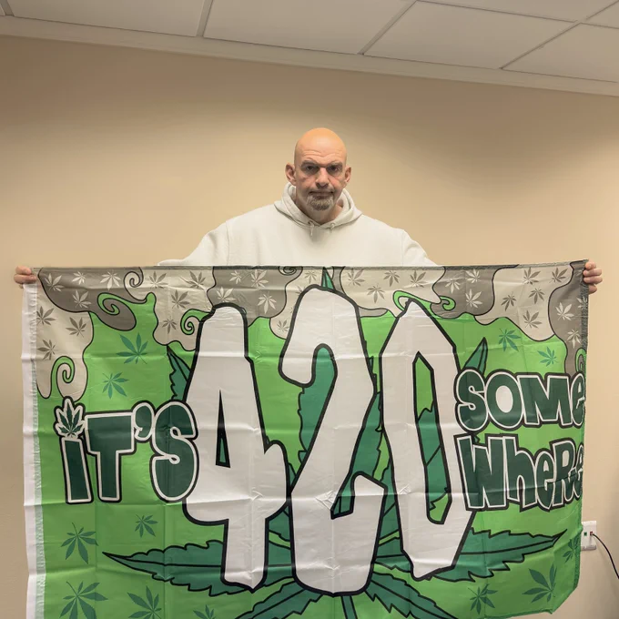 Senator Fetterman holding a green flag that says “It’s 420 somewhere”.