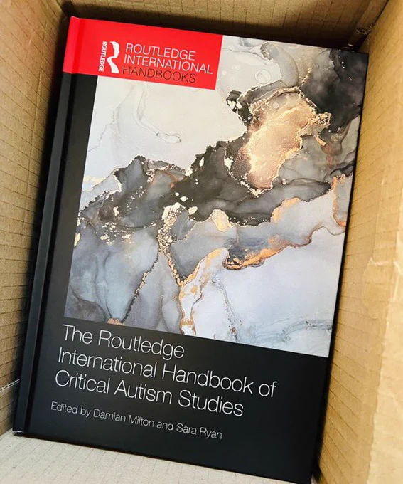Image of front cover of The Routledge International Handbook of Critical Autism Studies. An abstract image of what looks like grey and white marble with a gold thread throughout.