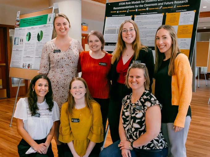 Seven research lab mentors posing by research poster