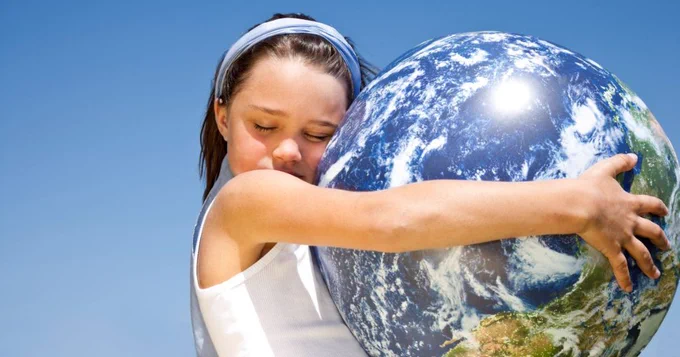 Little girl hugs a globe against a sky blue background