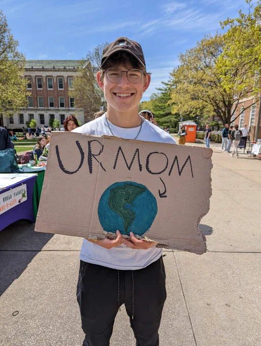 Photo of SECS student holding a sign that says, "Ur Mom" with a photo of the Earth. Credit: iSEE Communications