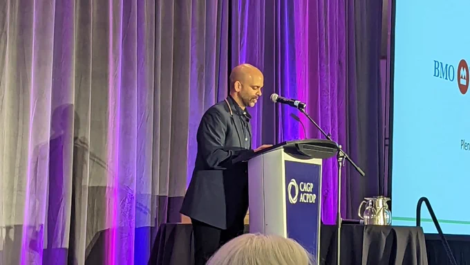 Aneil Gokhale wearing a suit and sharing at a podium which says CAGP