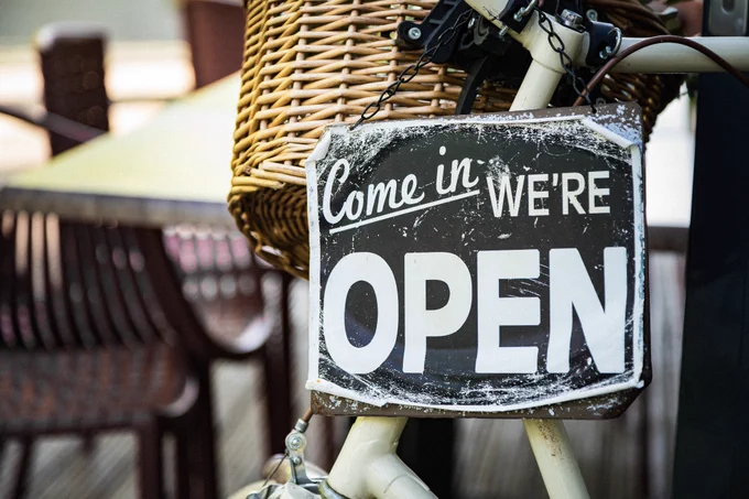 a bicycle has s sign on its a wicker basket. it says 'come in we're open'