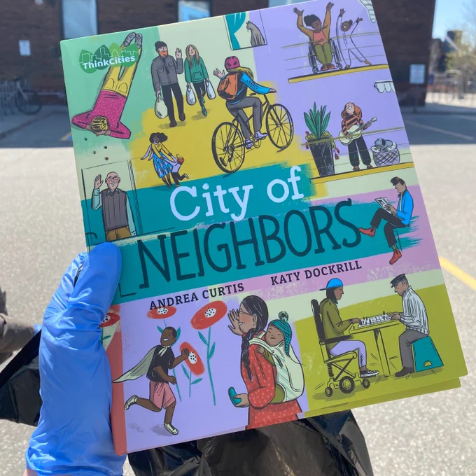 A photo of a hand wearing a blue glove holding up a copy of City of Neighbors.