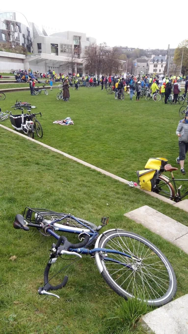 Bike on grass in foreground in front of Scottish Parliament building and cyclists 
