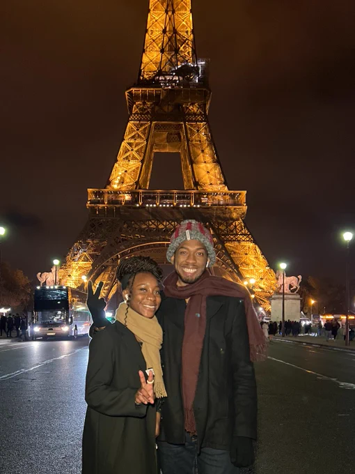 Two Beautiful Black people standing with the Eiffel Tower behind them. 