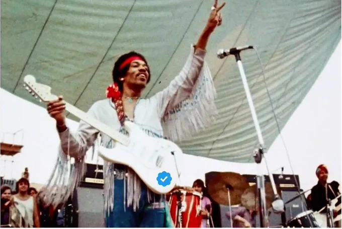 Jimi Hendrix at Woodstock. His guitar bears a blue Twitter verification badge.