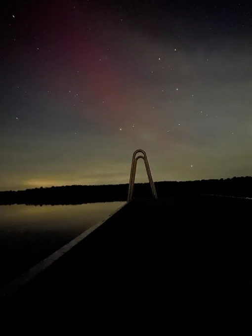 A handle for a ladder into a lake in the foreground; faint polar lights in green and red in the background. 