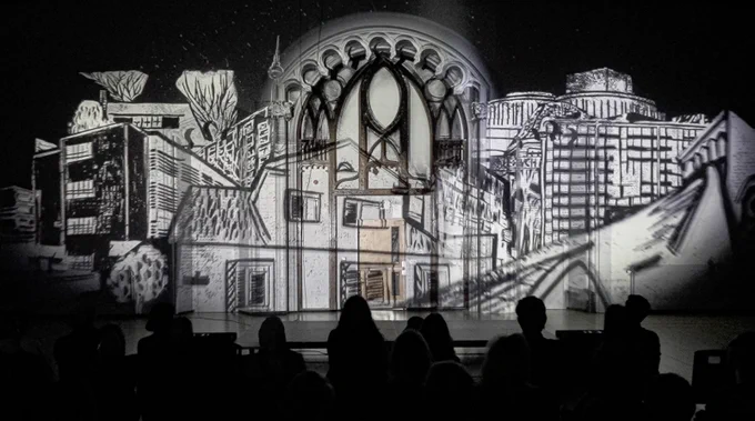 An audience is silhouetted against a wall-projected image of sketches of buildings.