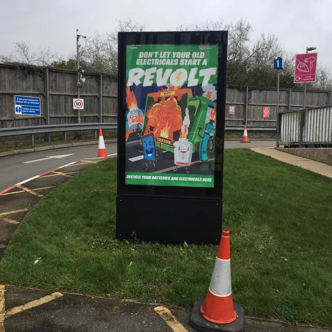 photo of a poster board outside a recycling centre. the poster contains and animated image of a dustcart on fire surrounded by batteries, vapes and mobile phones