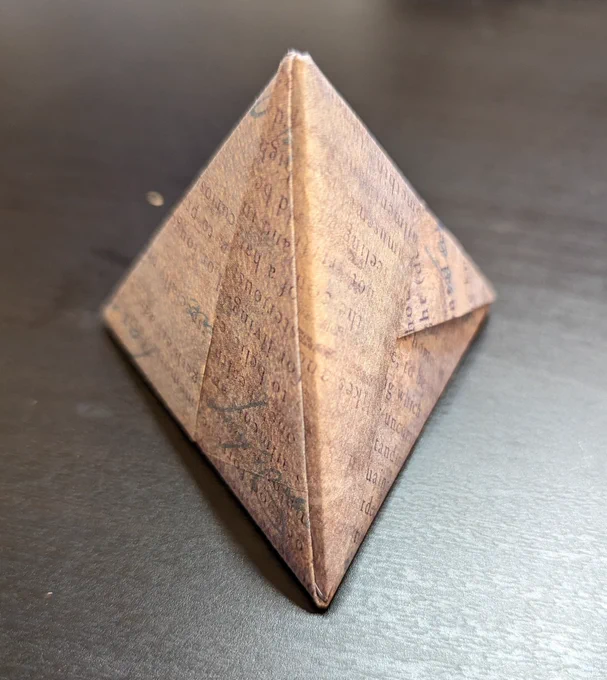Photo of Origami tetrahedron made of purple paper with abstract blocks of text, from one of the edges.