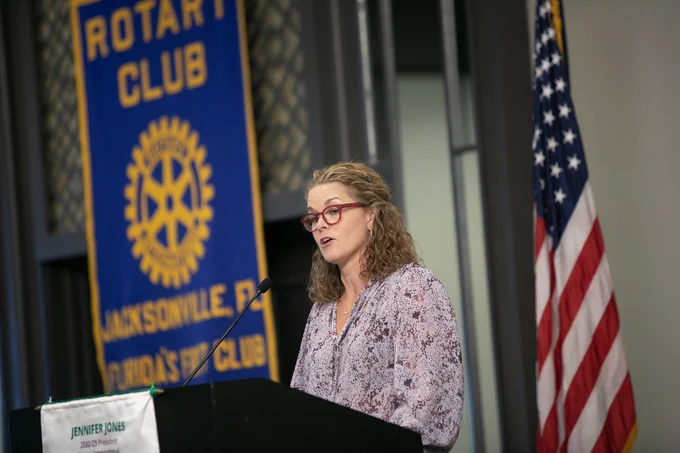 molly curry with a rotary club banner and an american flag in the background