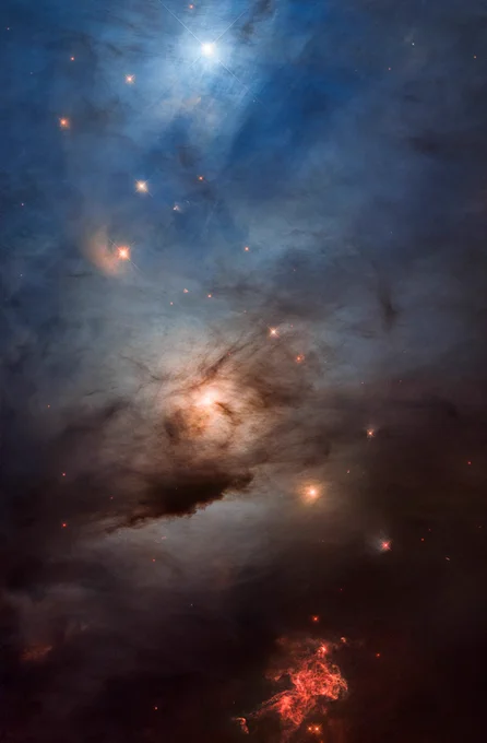  A vertical image with colors ranging from blue at the top to golden in the middle and red at the bottom. At the top, a bright blue star is illuminating surrounding clouds of gas, making the top third of the image appear blue. Below the bright star, a couple dozen fainter stars shine yellow. One of them has a fuzzy, golden arc to its left. At the center of the image, a brighter yellow star illuminates surrounding gas. It is partially obscured by dark streaks and clouds of dust, making it resemble the moon on a cloudy evening. The bottom of the image is noticeably darker than the rest, with the exception of a dramatic splash of red almost like a bug splat on a windshield. A handful of faint, red stars also appear there. Credit: NASA, ESA, and STScI; Image Processing: Varun Bajaj (STScI), Joseph DePasquale (STScI), Jennifer Mack (STScI)