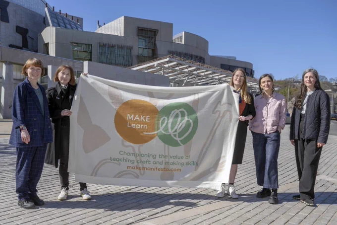 Members of the MAKE Learn team hold up the large MAKE Learn banner outside the Scottish Parliament building.
