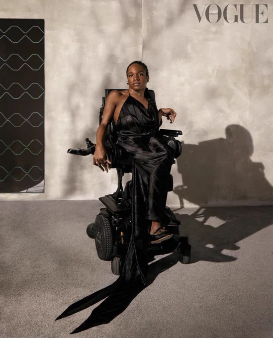 Aaron Philip wears a black silky dress and sits in a power chair.