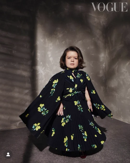 Sinéad Burke stands in a black and green cape dress.