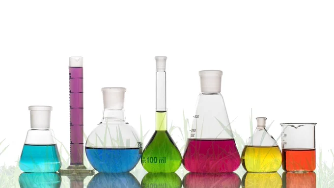 Chemistry flasks filled with different coloured liquids, over a grassy background.
