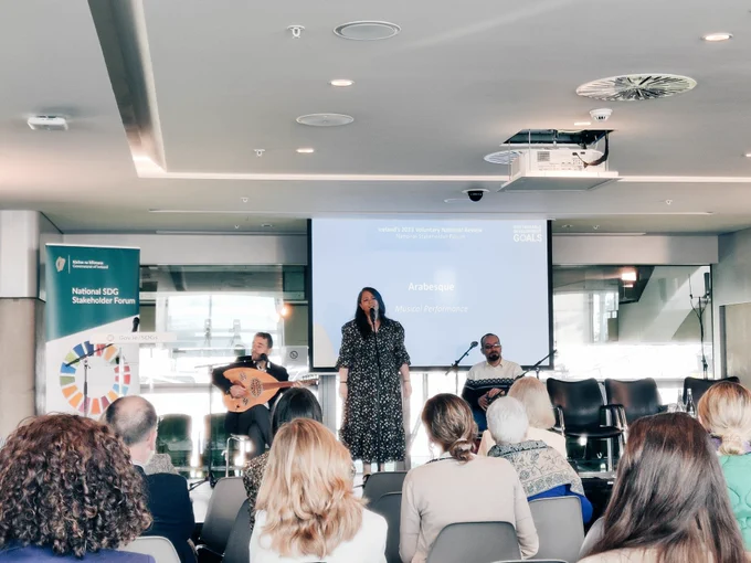 Photo of a crowd at Aviva stadium watching three performers on a stage in front of a projector screen.