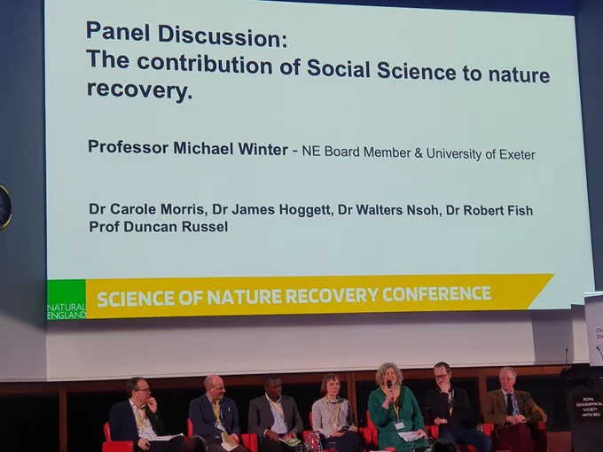 Seven social science experts sit in front of a large screen that reads: 'Panel discussion: The contribution of social science to nature recovery'.