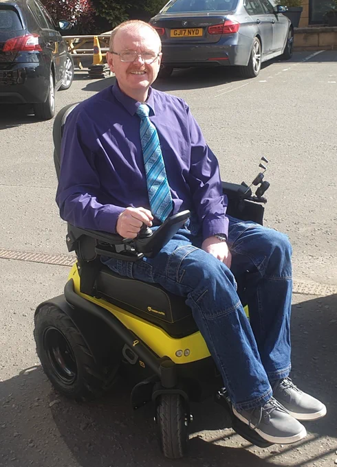 Michael pictured in his new, bright yellow, all-terrain, electric wheelchair.