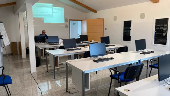 A training room with four rows of white desks.  There are two computers on each desk and empty blue chairs.