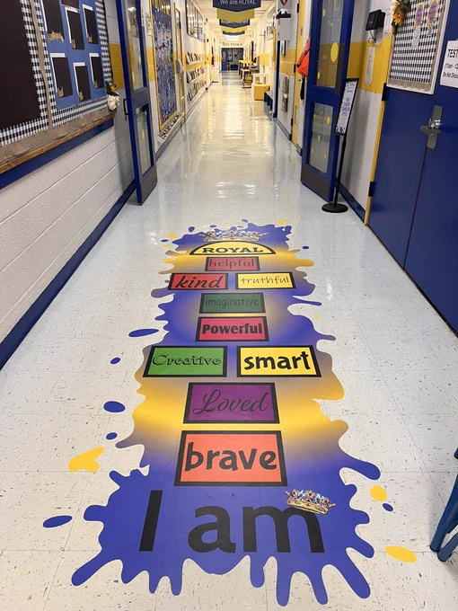 A hopscotch board painted on the floor in a school hallway. In front of the boards are painted the words, "I am," and the blocks in the board include adjectives such as brave, loved, creative and smart.
