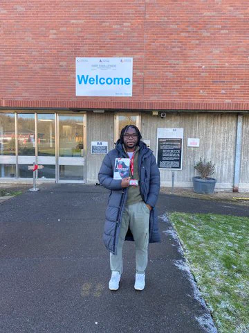 Author Yomi Sode standing infront of HMP Swaleside, holidng his book Mandem and looking into camera.