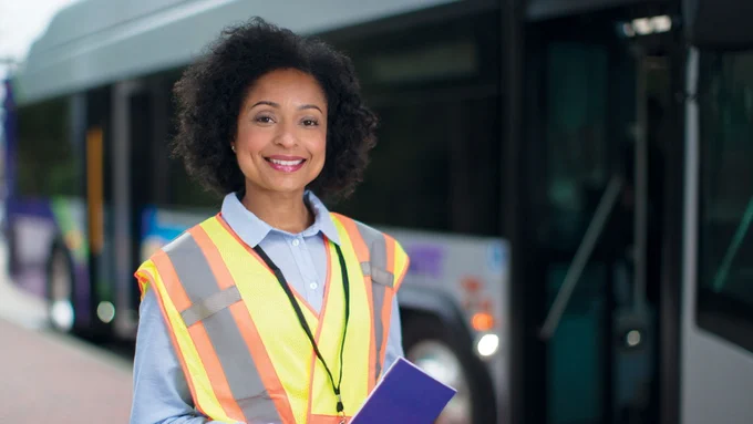 Person wearing a yellow safety vest holding information outside of a GRTC bus.