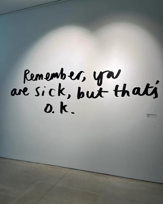 A white wall of the Turner Gallery which has been lit up. On it is the handwritten words: 'Remember, you are sick, but that's o.k.' - artwork by Lizzy Rose. 