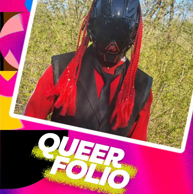 Head and shoulders of a human figure standing in front of green foliage. They wear a shiny black helmet, which covers their entire face. The helmet has a red triangle on the mouth and long red braids attached to the top of it. The figure also wears a red shirt, black suit jacket and black tie.