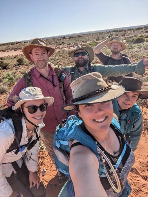 A group selfie of 6 scientists stood on the edge of a salt flat in the desert. There are three women and three men, and everyone is in field gear.