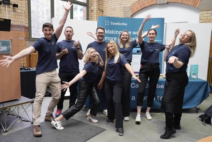 A photo of the CareScribe team smiling and jumping around the CareScribe stand with their arms in the air.