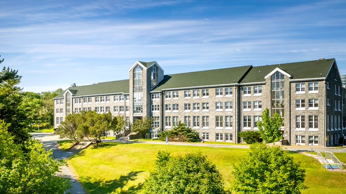 A drone photo of the Evaristus Hall building surrounded by lush green grass and trees, and a vibrant blue sky with wispy white clouds.
